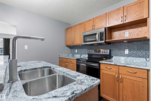 Kitchen featuring granite countertops, a double stainless steel sink with a modern faucet, wood cabinetry, and a mosaic tile backsplash - 1154 35A Avenue Nw, Edmonton, AB - Indoor Photo Showing Kitchen With Double Sink