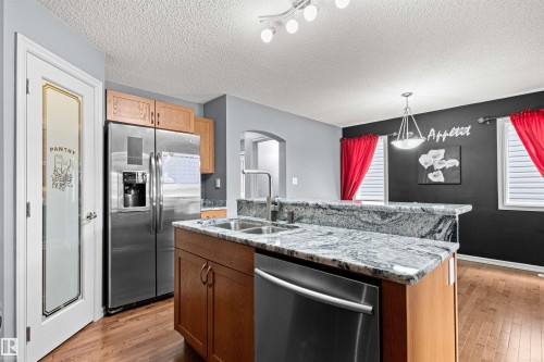 Kitchen featuring an island with a double basin sink, granite countertops, wood cabinetry, and stainless steel appliances - 1154 35A Avenue Nw, Edmonton, AB - Indoor Photo Showing Kitchen With Double Sink