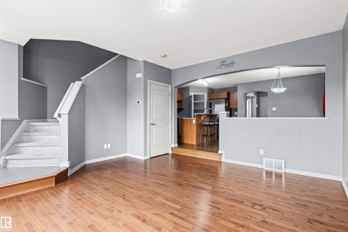 Spacious interior featuring wood-finish flooring, a carpeted staircase with white risers, and a functional half-wall with an arched opening - 1154 35A Avenue Nw, Edmonton, AB - Indoor Photo Showing Other Room