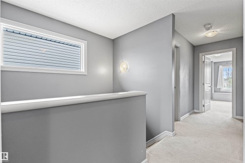 Carpeted hallway featuring a rectangular window with horizontal blinds, a wall sconce, and white trim - 1154 35A Avenue Nw, Edmonton, AB - Indoor Photo Showing Other Room