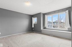 Carpeted interior room featuring a large window with a built-in window seat, a smaller casement window, gray wall paint, and a ceiling-mounted light fixture - 