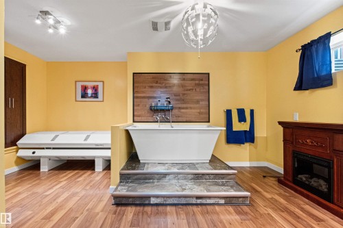 Freestanding soaking tub on a raised tile platform with a wood-paneled accent wall - 1154 35A Avenue Nw, Edmonton, AB - Indoor With Fireplace