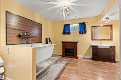 Bathroom featuring a freestanding white tub with a wood-panel accent wall, warm yellow paint, wood-finish flooring, a vanity with a rectangular sink, and a decorative fireplace - 