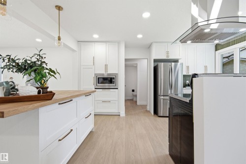 Modern kitchen featuring white shaker cabinetry, stainless steel appliances, a range hood, and light wood-finish flooring - 14335 47 Avenue Nw, Edmonton, AB - Indoor Photo Showing Kitchen With Upgraded Kitchen