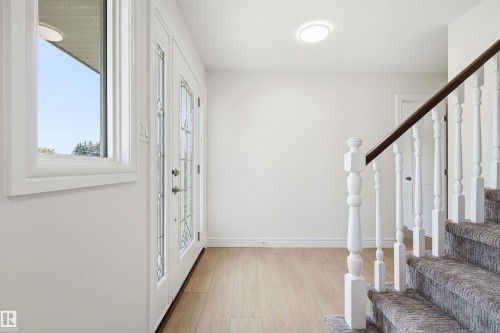 Entryway featuring light wood-finish flooring, white walls, and a staircase with a dark wood handrail and white balusters - 14335 47 Avenue Nw, Edmonton, AB - Indoor Photo Showing Other Room