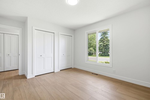 Bright room featuring a large window, light wood-finish flooring, white walls, and multiple bi-fold closet doors - 14335 47 Avenue Nw, Edmonton, AB - Indoor Photo Showing Other Room