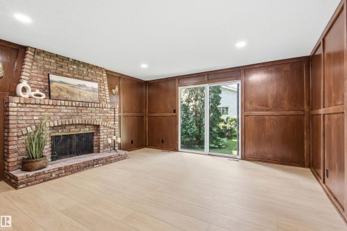 Brick fireplace with an arched firebox, wood-finish flooring, recessed lighting, and rich wood paneling with integrated cabinetry - 14335 47 Avenue Nw, Edmonton, AB - Indoor With Fireplace