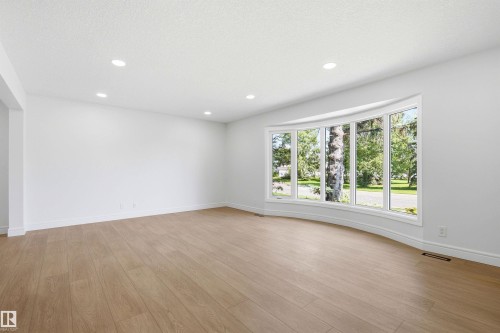 Expansive main living area featuring a curved bay window, recessed ceiling lighting, light wood-finish flooring, and crisp white walls - 14335 47 Avenue Nw, Edmonton, AB - Indoor Photo Showing Other Room