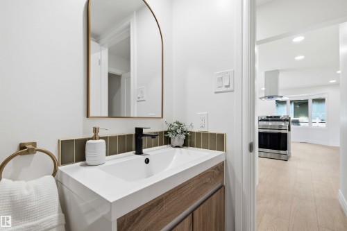 Modern vanity featuring a wood-finish base, integrated sink, and matte black faucet - 14335 47 Avenue Nw, Edmonton, AB - Indoor Photo Showing Bathroom