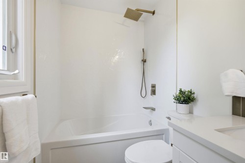 White bathtub and shower combination featuring a rain showerhead and handheld shower fixture - 14335 47 Avenue Nw, Edmonton, AB - Indoor Photo Showing Bathroom