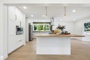 Modern kitchen featuring a large center island with a light wood-finish countertop, white cabinetry with bronze hardware, and wood-finish flooring - 14335 47 Avenue Nw, Edmonton, AB  - Indoor Photo Showing Kitchen With Upgraded Kitchen 