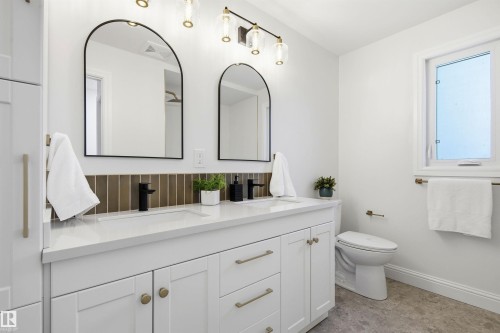 Double vanity featuring white shaker cabinetry with brass hardware, quartz countertop, and rectangular undermount sinks - 14335 47 Avenue Nw, Edmonton, AB - Indoor Photo Showing Bathroom