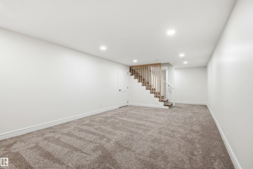 Open concept room featuring recessed lighting, light gray textured carpet, white baseboards, and a wooden staircase with white risers - 14335 47 Avenue Nw, Edmonton, AB - Indoor
