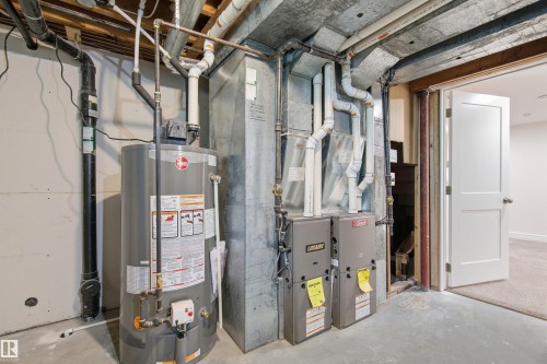Basement utility area featuring a water heater, dual furnaces, exposed ductwork, and concrete flooring - 14335 47 Avenue Nw, Edmonton, AB - Indoor Photo Showing Basement