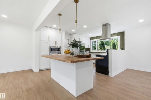 Kitchen featuring a central island with a wood-finish countertop, white cabinetry with gold-finish hardware, stainless steel microwave, and a range hood - 14335 47 Avenue Nw, Edmonton, AB - Indoor Photo Showing Kitchen With Upgraded Kitchen