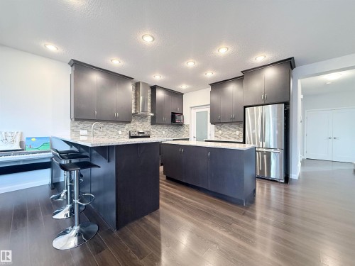 Contemporary kitchen featuring dark wood-finish cabinetry, stainless steel appliances, speckled countertops, and a mosaic tile backsplash - 5876 168 Avenue Nw, Edmonton, AB - Indoor Photo Showing Kitchen With Upgraded Kitchen