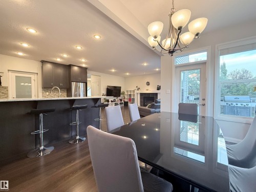 Dining area featuring a dark glossy table, overhead chandelier, and multiple windows - 5876 168 Avenue Nw, Edmonton, AB - Indoor Photo Showing Dining Room