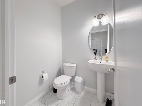 Powder room featuring a pedestal sink, a wall-mounted oval mirror, and a two-bulb vanity light fixture - 5876 168 Avenue Nw, Edmonton, AB - Indoor Photo Showing Bathroom