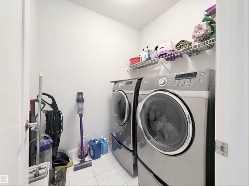 Dedicated laundry space featuring a side-by-side washer and dryer set, white wire shelving, and tiled flooring - 5876 168 Avenue Nw, Edmonton, AB - Indoor Photo Showing Laundry Room