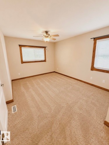 Carpeted room featuring multiple windows with wood-trim surrounds and a ceiling fan with integrated lighting - 610 8 Avenue, Wainwright, AB - Indoor Photo Showing Other Room