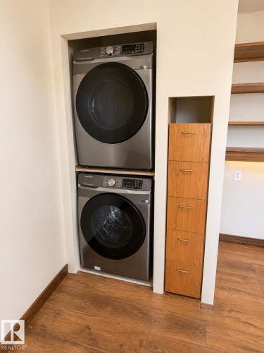 Stacked washer and dryer units featuring a wood-finish flooring - 610 8 Avenue, Wainwright, AB - Indoor Photo Showing Laundry Room