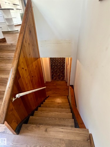 Staircase featuring wood-finish treads and risers, a wood-paneled wall, and a wood handrail with a white metal accent - 610 8 Avenue, Wainwright, AB - Indoor Photo Showing Other Room
