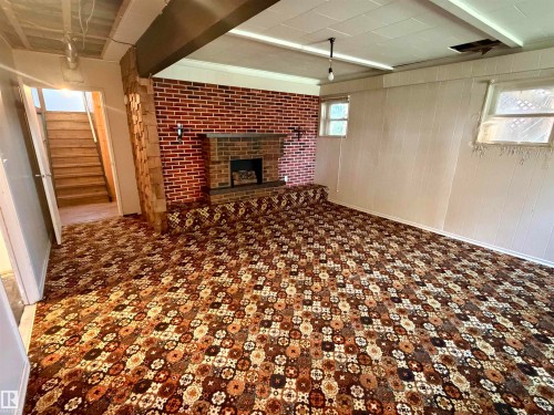 Spacious room featuring a brick fireplace, built-in hearth, paneled walls, and patterned carpet flooring - 610 8 Avenue, Wainwright, AB - Indoor