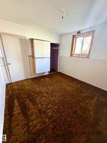 Room featuring brown textured carpeting, white wall paneling, and a single window with wood framing - 610 8 Avenue, Wainwright, AB - Indoor Photo Showing Other Room