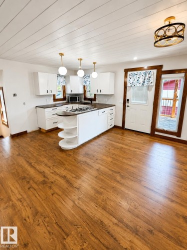 Spacious kitchen featuring wood-finish flooring, white cabinetry, and dark countertops - 610 8 Avenue, Wainwright, AB - Indoor