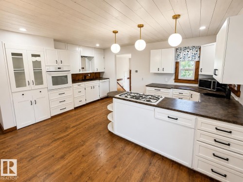 Spacious kitchen featuring an expansive island with a built-in gas cooktop, white cabinetry, dark countertops, wood-finish flooring, and a white plank ceiling - 610 8 Avenue, Wainwright, AB - Indoor Photo Showing Kitchen With Double Sink