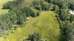 Expansive green acreage featuring a large clearing, mature trees, dense wooded areas, and a small outbuilding - 