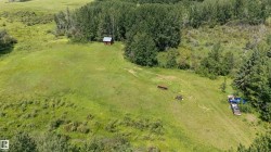 Expansive green space featuring a small cabin with a metal roof and surrounding mature trees - 