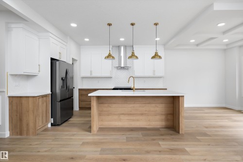 Contemporary kitchen featuring a large central island, white shaker cabinetry, wood-finish lower cabinetry, a herringbone tile backsplash, and recessed lighting - 919 Elderberry Landing Nw, Edmonton, AB - Indoor Photo Showing Kitchen With Upgraded Kitchen