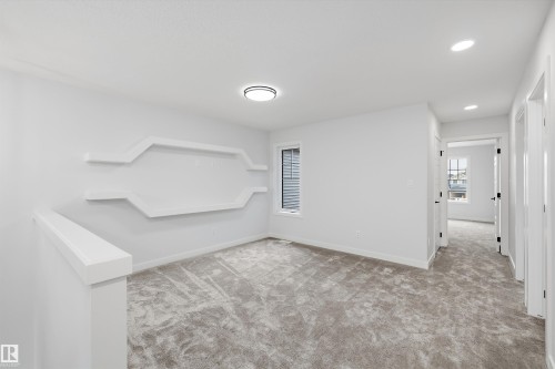 Carpeted landing area featuring a decorative architectural wall with integrated shelving, a large window with blinds, recessed lighting, and a contemporary flush-mount light fixture - 919 Elderberry Landing Nw, Edmonton, AB - Indoor Photo Showing Other Room