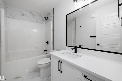 Contemporary bathroom featuring a white tub/shower combination with a marble-look tile surround, a white vanity with a rectangular undermount sink, a large framed mirror, and matte black fixtures - 919 Elderberry Landing Nw, Edmonton, AB - Indoor Photo Showing Bathroom