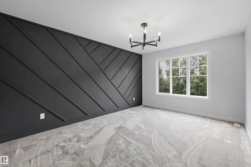 Accent wall featuring geometric paneling, contemporary chandelier, large window with grid pattern, light gray carpeting, and neutral wall paint - 919 Elderberry Landing Nw, Edmonton, AB - Indoor Photo Showing Other Room
