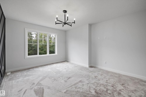 Spacious room featuring a large multi-pane window, contemporary chandelier, light gray carpeting, and white baseboards - 919 Elderberry Landing Nw, Edmonton, AB - Indoor Photo Showing Other Room