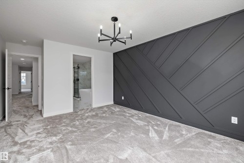 Spacious room featuring a decorative accent wall with geometric paneling, light gray carpeting, and a modern black chandelier - 919 Elderberry Landing Nw, Edmonton, AB - Indoor Photo Showing Other Room