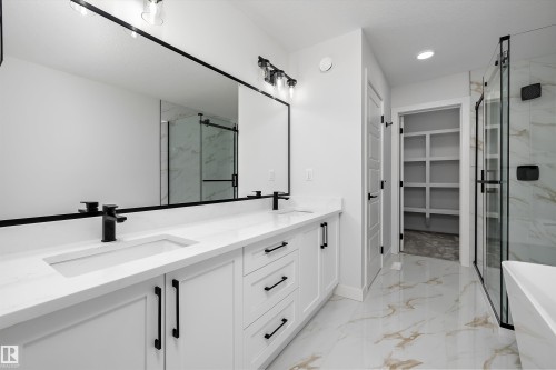 Dual vanity with white cabinetry and matte black hardware, stone-finish countertops, and under-mount sinks - 919 Elderberry Landing Nw, Edmonton, AB - Indoor Photo Showing Bathroom