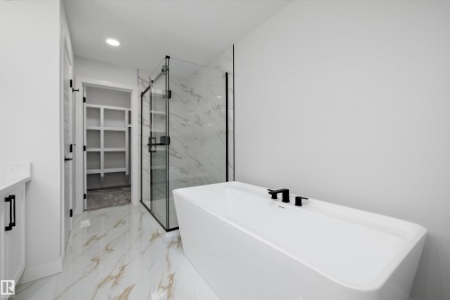 Freestanding soaking tub featuring matte black fixtures, set against a frameless glass shower enclosure with marble-look tile - 919 Elderberry Landing Nw, Edmonton, AB - Indoor Photo Showing Bathroom