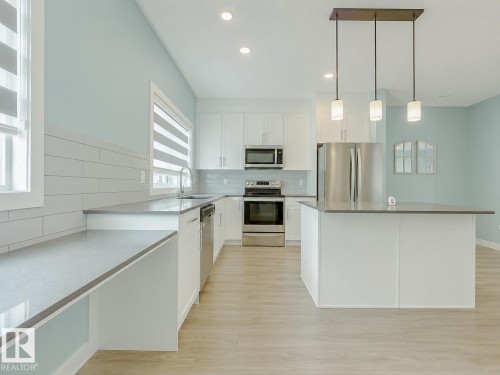 Modern kitchen featuring white cabinetry, stainless steel appliances, a center island with pendant lighting, light wood-finish flooring, and subway tile backsplash - #56 804 Welsh Dr Sw, Edmonton, AB - Indoor Photo Showing Kitchen With Stainless Steel Kitchen With Upgraded Kitchen