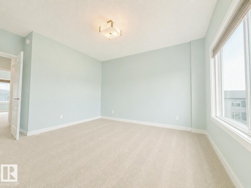 Spacious room featuring light blue walls, soft neutral carpeting, a large window, white trim throughout, and a flush-mount ceiling light fixture - #56 804 Welsh Dr Sw, Edmonton, AB - Indoor Photo Showing Other Room
