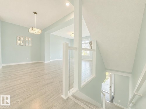 Open-concept interior featuring light wood-finish flooring, a contemporary pendant light fixture, recessed ceiling lighting, and a glass-paneled staircase railing - #56 804 Welsh Dr Sw, Edmonton, AB - Indoor Photo Showing Other Room