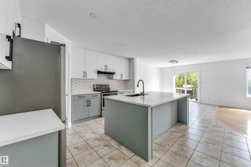 Modern kitchen featuring a large central island with a sink and gooseneck faucet, two-tone cabinetry, subway tile backsplash, and stainless steel appliances - 16205 55 Street Nw, Edmonton, AB - Indoor Photo Showing Kitchen With Upgraded Kitchen
