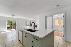 Central kitchen island with a double basin sink and matte black faucet, featuring an integrated dishwasher and light green cabinetry with matte black hardware - 