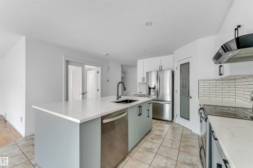 Kitchen featuring a large central island with light-toned countertop, stainless steel appliances, white cabinetry, and tile flooring - 16205 55 Street Nw, Edmonton, AB - Indoor Photo Showing Kitchen With Upgraded Kitchen