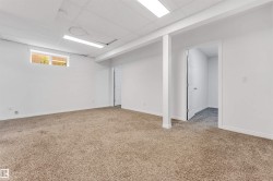 Spacious room featuring neutral carpeting, white walls, and a drop ceiling with integrated fluorescent lighting - 