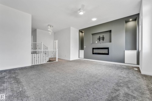 Spacious room featuring gray carpeting, an accent wall with a built-in electric fireplace, recessed lighting, and wall niches with integrated illumination - 16205 55 Street Nw, Edmonton, AB - Indoor With Fireplace