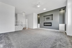 Spacious room featuring gray carpeting, an accent wall with a built-in electric fireplace, recessed lighting, and wall niches with integrated illumination - 