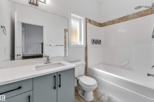 Bathroom featuring a spacious vanity with a white countertop and gray cabinetry, an integrated sink with a chrome faucet, a large wall-mounted mirror, and a tub/shower combination with a tiled surround - 16205 55 Street Nw, Edmonton, AB - Indoor Photo Showing Bathroom